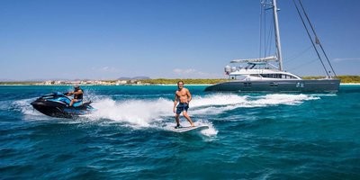man on surfboard, man on jetski, next to silver catamaran in the maldives