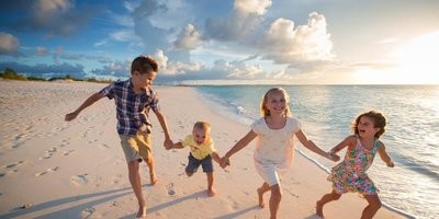 Four children running along a beach, laughing and holding hands