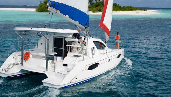 Man and woman sailing catamaran towards a Maldives island